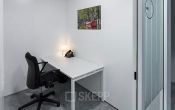 Interior of office space rental at Willemsplein 2, Den Bosch with a white desk, black chair, desk lamp, phone, and wall art.