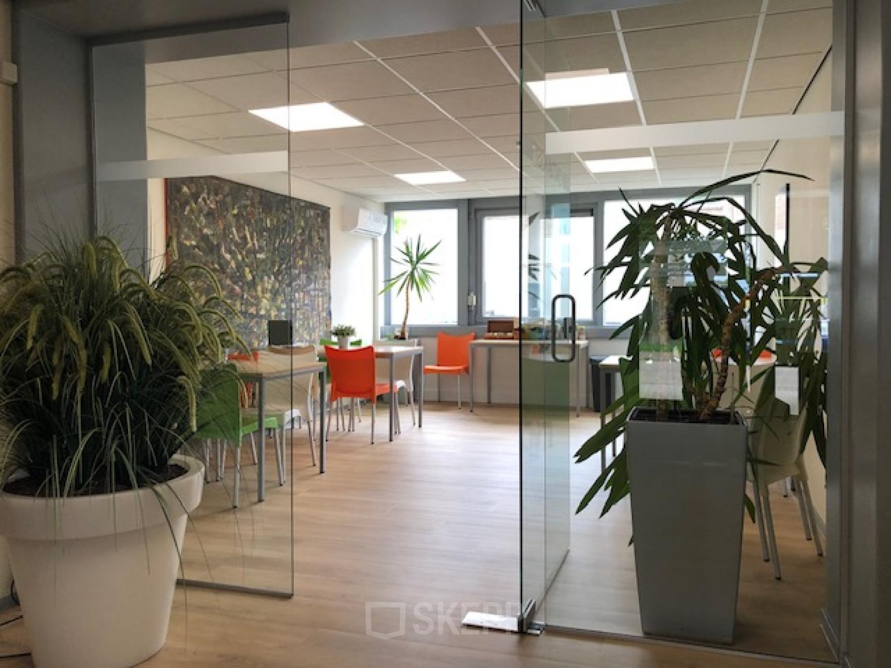 Bright and modern office space at Eemweg 1-9, Den Bosch, with large potted plants and colorful chairs around desks.