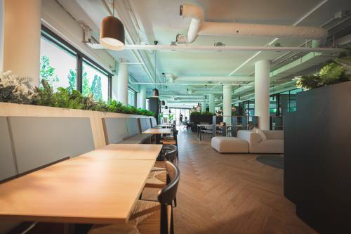Modern workspace at Hambakenwetering 1, Den Bosch, featuring sleek wooden tables, lounge seating, and ample greenery. Ideal for those seeking office space rental in a vibrant environment.