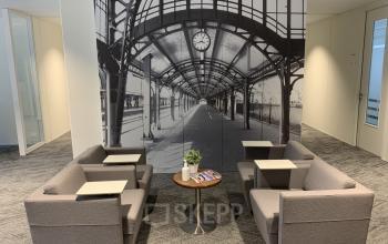 Contemporary office space rental at Stationsplein 91, Den Bosch, featuring comfortable seating and a wall mural depicting a train station.