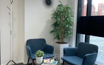 Modern lounge area in an office to rent at Stationsplein 91, Den Bosch, featuring comfortable blue armchairs and greenery.