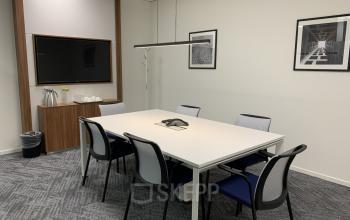 Neatly organized office space rental at Stationsplein 91, Den Bosch, with a white conference table, comfortable chairs, and a mounted TV for presentations.