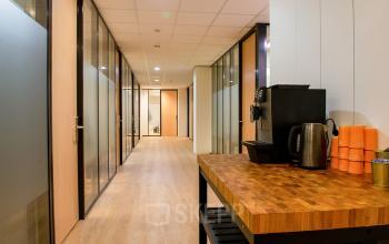 Interior view of an office hallway at Bruistensingel 400, Den Bosch, featuring wooden flooring, glass doors, and a coffee station. Ideal for office space rental opportunities.
