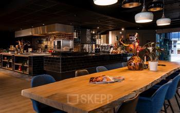 Modern office space at Bruistensingel 400, Den Bosch, featuring a stylishly furnished lounge area with a wooden table and kitchen amenities, ideal for office space rental.