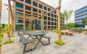Outdoor seating area with wooden pergola and modern office building at Hambakenwetering 1-kr, Den Bosch, ideal for office space rental.