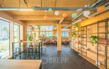 Bright, spacious office space with modern decor and natural wood tones in Den Bosch, ready for rental. Features include stylish shelving, large windows, and vibrant furnishings.