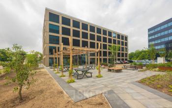 Modern office building at Hambakenwetering 1-kr, Den Bosch, featuring a spacious exterior with outdoor seating and landscaped gardens, ideal for those seeking office space rental.