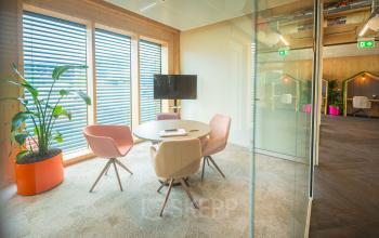 Bright office space with round table, modern chairs, large windows, and a TV for presentations, located at Hambakenwetering 1-kr in Den Bosch, ideal for office space rental.
