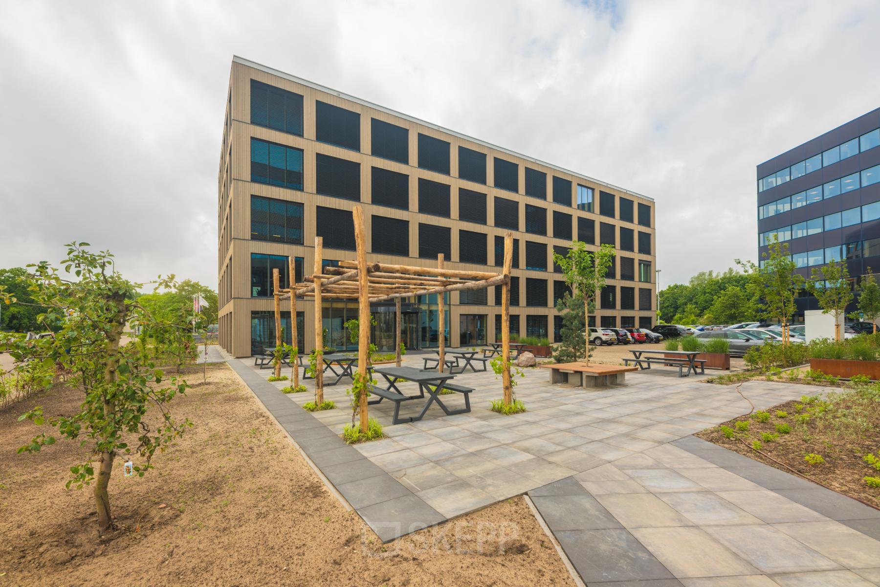 Modern office building at Hambakenwetering 1-kr, Den Bosch, featuring a spacious exterior with outdoor seating and landscaped gardens, ideal for those seeking office space rental.