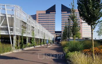 Exterior view of the office building at Utopialaan 22, Den Bosch, showcasing its modern architecture and adjacent parking facilities, available for office space rental.