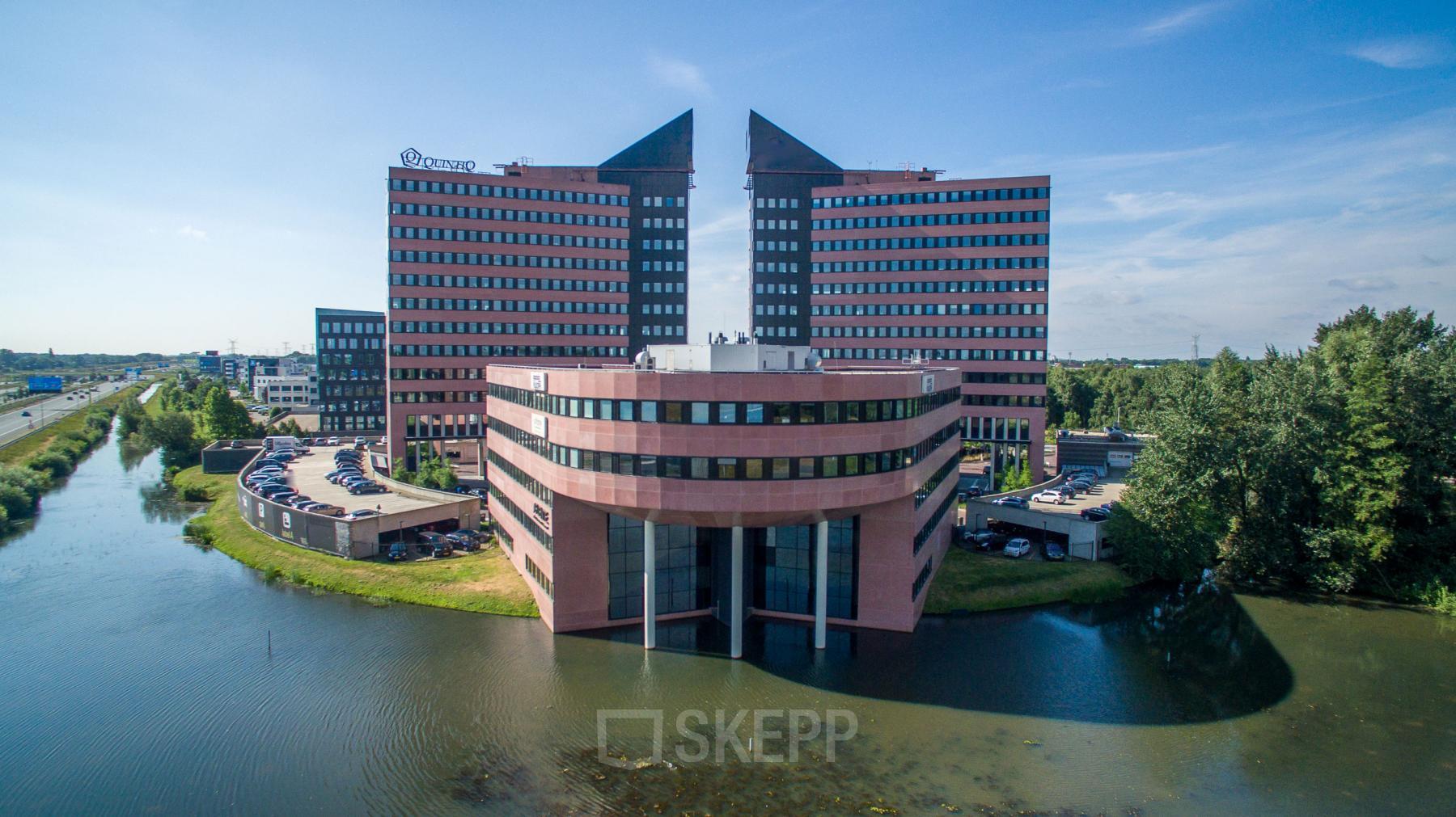 Modern office building at Utopialaan 22, Den Bosch, surrounded by water and greenery, showcasing a unique architectural design, available as an office space rental.