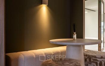 A cozy office seating area in Pettelaarpark 110, Den Bosch, featuring a round table and cushioned stools under subtle lighting. Ideal for informal meetings or casual relaxation.