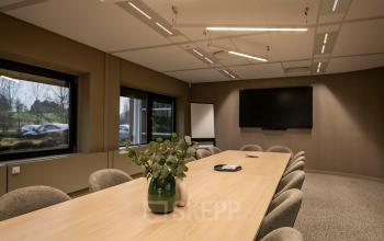 Modern conference room at Pettelaarpark 110, Den Bosch, featuring a long wooden table, plush chairs, and a large screen, ideal for productive meetings and office space rental.