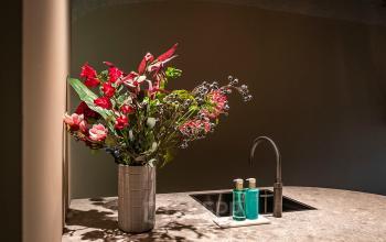 A stylish kitchenette at Pettelaarpark 110, Den Bosch, featuring a sleek countertop, modern faucet, floral arrangement, and premium toiletries, perfect for office space rental.