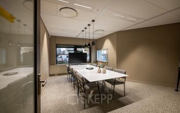 Modern conference room with a large table and chairs, pendant lights, and a TV screen, perfect for meetings. Located at Pettelaarpark 110, Den Bosch, offering office space rental.