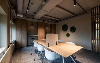 Modern office space with natural lighting, featuring a wooden meeting table, white chairs, and decorative wall accents, located at Pettelaarpark 110, Den Bosch, ideal for office space rental.