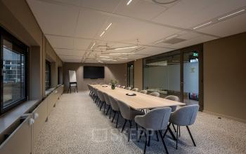 Modern conference room at Pettelaarpark 110 in Den Bosch with a long table, comfortable chairs, large windows, and a presentation screen, ideal for office space rental.