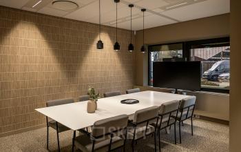 Modern conference room with a long white table, eight chairs, and large screen, located at Pettelaarpark 110, Den Bosch. Ideal for office space rental meetings, featuring subtle lighting and a contemporary design.