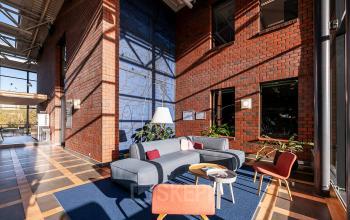 Spacious and bright lounge area with modern seating and large windows in an office space rental at Hambakenwetering 5, Den Bosch. Features red brick walls and blue carpet accents.
