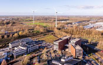 Aerial view of the office buildings at Hambakenwetering 5 in Den Bosch, surrounded by greenery and parking spaces. Ideal location for office space rental with nearby wind turbines and open landscapes.