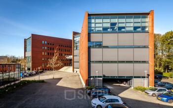 Exterior view of the office building at Hambakenwetering 5, Den Bosch, showcasing modern architecture with large glass windows. Ample parking is visible in the foreground, ideal for office space rental.