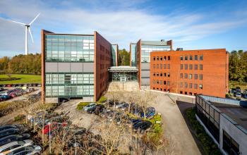 Exterior view of the office space rental at Hambakenwetering 5, Den Bosch. The modern office building features large glass windows and ample parking space, providing a professional setting for businesses.