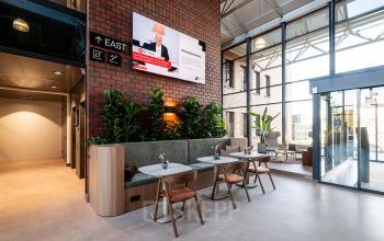 Modern office space at Hambakenwetering 5 in Den Bosch with stylish furnishings, indoor plants, and a wall-mounted screen. Perfect for office space rental, it features natural lighting and a comfortable seating area.