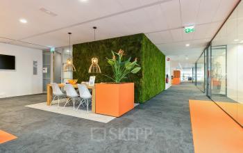 Modern office interior at Hambakenwetering 5 in Den Bosch with stylish décor featuring a green wall, wooden table, and white chairs. Ideal for office space rental.