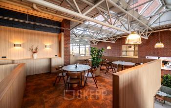 Furnished office space with round tables and chairs under large skylights at Hambakenwetering 5, Den Bosch, ideal for office space rental.