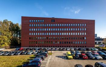 Exterior view of office building at Hambakenwetering 5, Den Bosch, featuring a red brick facade and ample parking space. Ideal office space rental opportunity with convenient accessibility.
