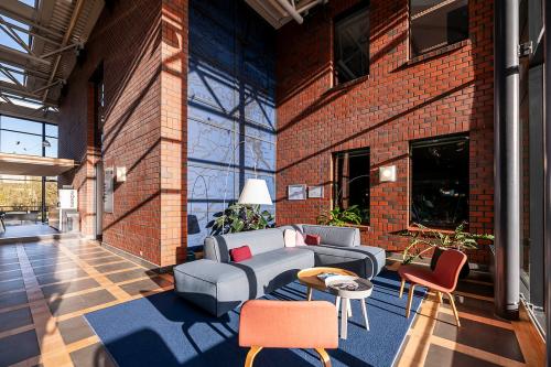 Spacious and bright lounge area with modern seating and large windows in an office space rental at Hambakenwetering 5, Den Bosch. Features red brick walls and blue carpet accents.