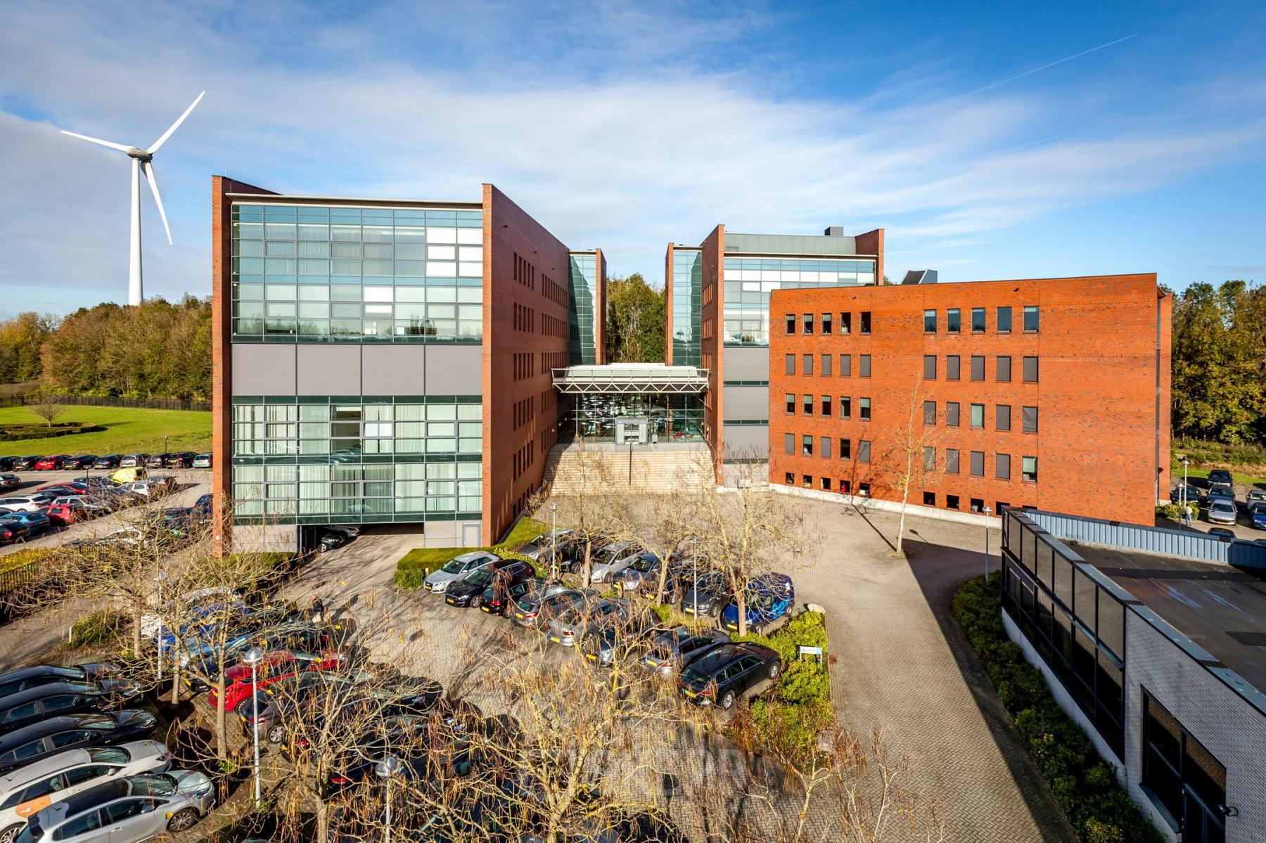 Exterior view of the office space rental at Hambakenwetering 5, Den Bosch. The modern office building features large glass windows and ample parking space, providing a professional setting for businesses.