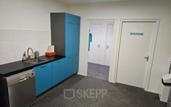 Compact pantry with blue cabinets and a sink, located at Hambakenwetering 18, Den Bosch. Ideal office space rental for those needing functional amenities. Adjacent door labeled 'DOUCHE.'