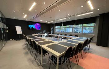 Modern conference room at Bruistensingel 500, Den Bosch with large U-shaped table setup, comfortable chairs, and a digital screen, ideal for office space rental. Well-lit with natural light from large windows.