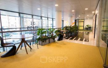 Spacious office interior at Bruistensingel 500, Den Bosch features large windows, modern seating, and greenery, providing an inviting work environment. Perfect for those seeking office space rental with natural light.
