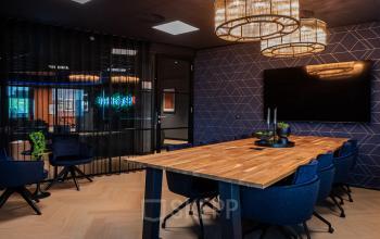 Modern conference room available for office space rental at Reitschweg 1, Den Bosch, featuring a wooden table, blue chairs, and stylish lighting.
