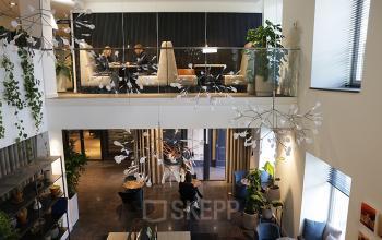 Elevated view of a modern Koninginnegracht 19 office space rental in The Hague Center, with business professionals in a meeting and others at workstations.