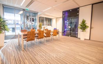 Modern office space rental at Koningin Julianaplein 10, The Hague Center, featuring a spacious interior with wooden chairs around a table and greenery enhancing the ambiance.