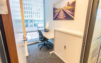 Compact office space at Koningin Julianaplein 10 in The Hague Center, featuring a desk, chair, and cabinet, ideal for office space rental with natural light from large window.