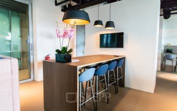 Modern office space with high stools at a wooden table, beneath sleek pendant lighting, in The Hague Center. Ideal for rent as a workspace with a cozy setup for meetings.