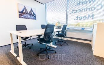 Furnished office space rental at Koningin Julianaplein 10, The Hague Center, featuring a meeting table and chairs with city views from large windows.
