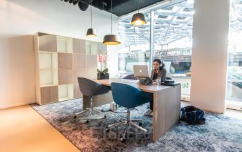 Bright office space at Koningin Julianaplein 10, The Hague Center featuring a modern desk, chairs, and a person working on a laptop. Ideal for office space rental needs.