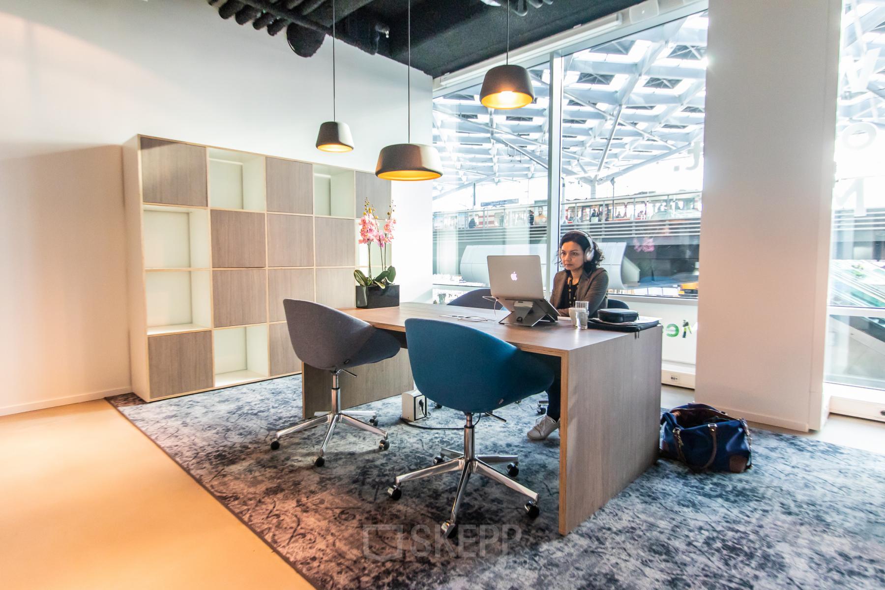 Bright office space at Koningin Julianaplein 10, The Hague Center featuring a modern desk, chairs, and a person working on a laptop. Ideal for office space rental needs.