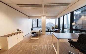 Modern furnished office space to rent at Anna van Buerenplein 41, The Hague Center, featuring well-lit workstations with large windows offering city views.