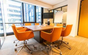 Bright office space available for rent at Anna van Buerenplein 41 in The Hague Center, featuring a modern conference room with orange chairs around a wooden table and large windows.