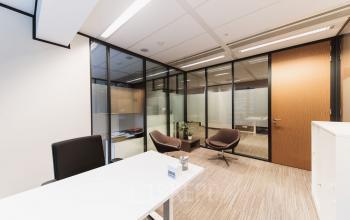 Bright office space with glass walls at Anna van Buerenplein 41, The Hague Center, available for rent. Features modern furniture, including a desk and chairs, enhancing office space rental appeal.