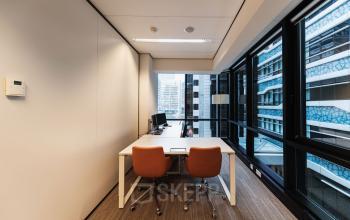 Modern office space for rent at Anna van Buerenplein 41, featuring a bright room with a large window, two chairs, and a work table in The Hague Center.