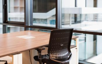 Bright office space with a desk and ergonomic chair, featuring floor-to-ceiling windows offering a view of The Hague Center. Ideal for office space rental.