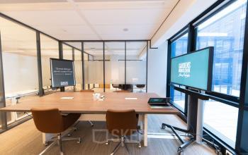 Modern office space to rent at Anna van Buerenplein 41, The Hague Center, featuring a furnished meeting area with digital displays and large windows.