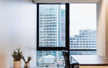 Furnished office space at Anna van Buerenplein 41, The Hague Center, featuring a desk, chair, and a view of the city through large windows; available for rent.
